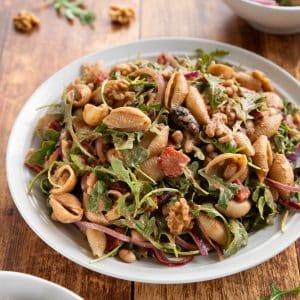 A no-mayo Italian pasta salad with white beans, arugula, roasted red peppers, and kalamata olives, tossed in an oil-free sundried tomato balsamic dressing with toasted walnuts and fennel