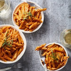 Vegan penne alla vodka in a sauté pan, tossed in creamy pink cashew vodka sauce and topped with fresh basil