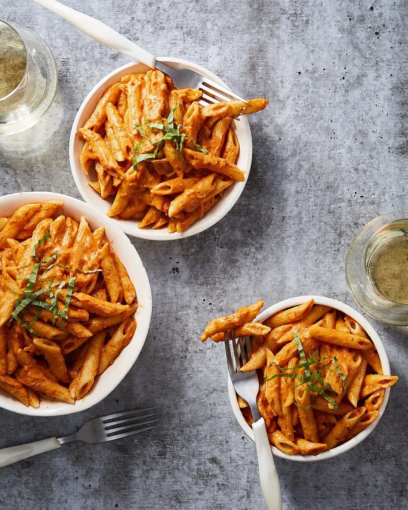 Vegan penne alla vodka in a sauté pan, tossed in creamy pink cashew vodka sauce and topped with fresh basil